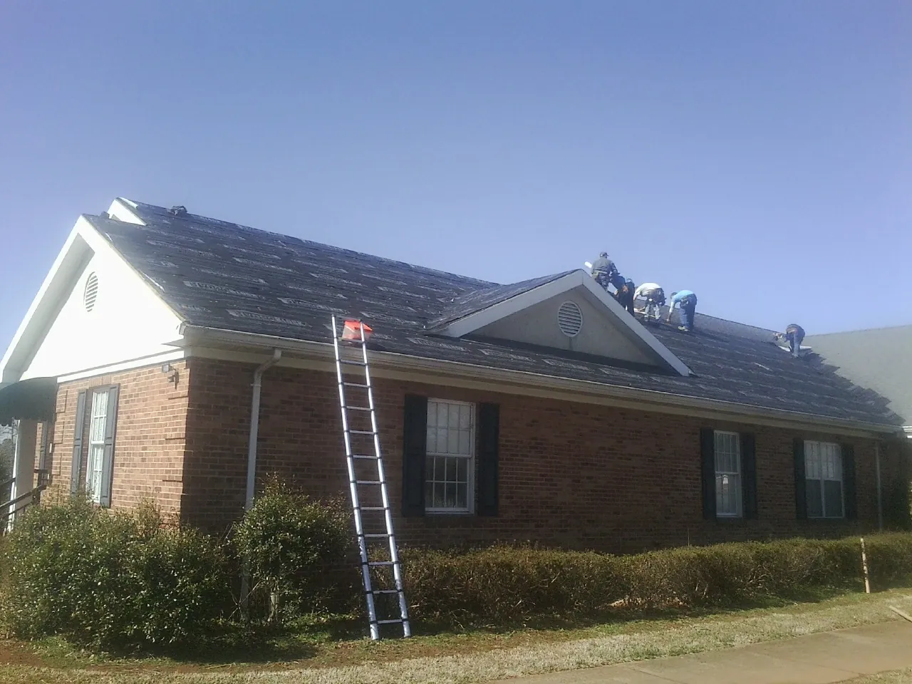 Crew tearing shingles off a brick ranch roof with a ladder set — Metal Roof Repair work by our crew in Fillmore